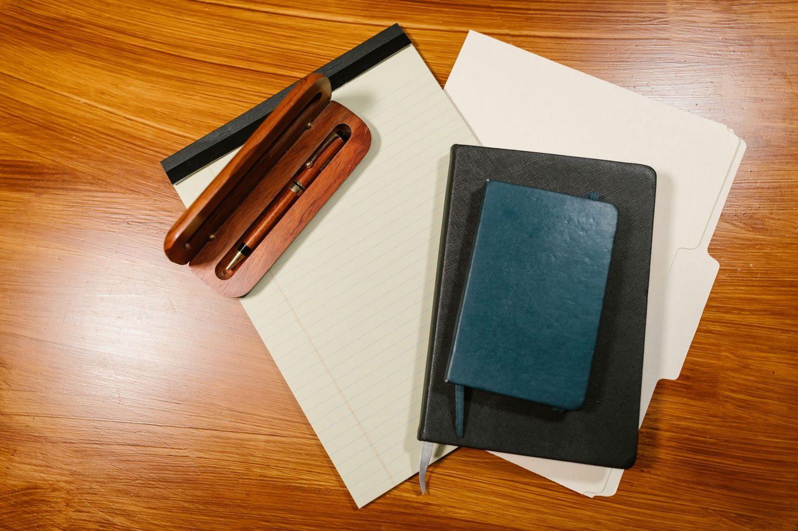 A pen in a wooden case on a lined pad beside notebooks and a manila folder